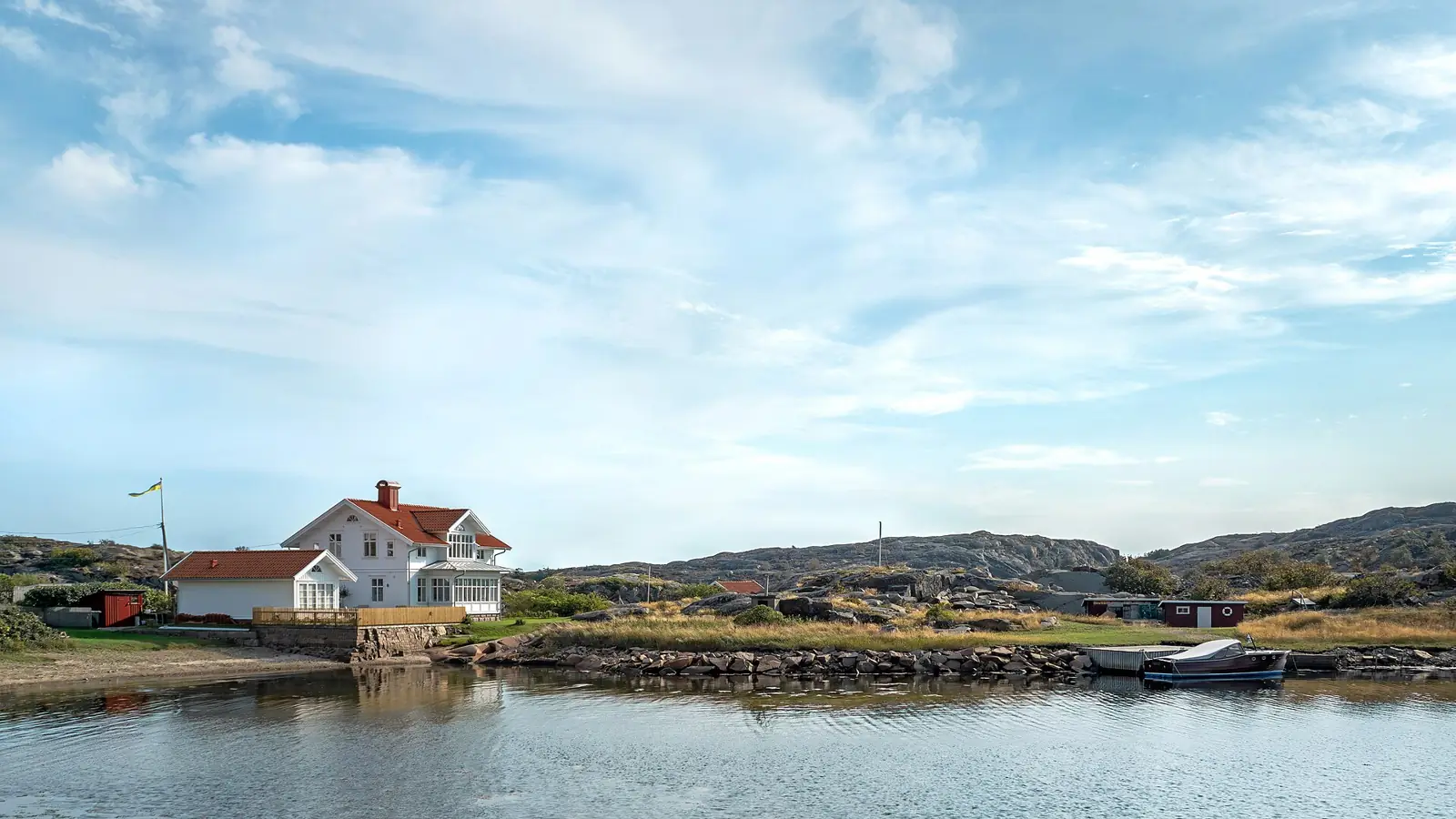Vitt hus vid vattnet på västkusten med klippor och sjöbodar