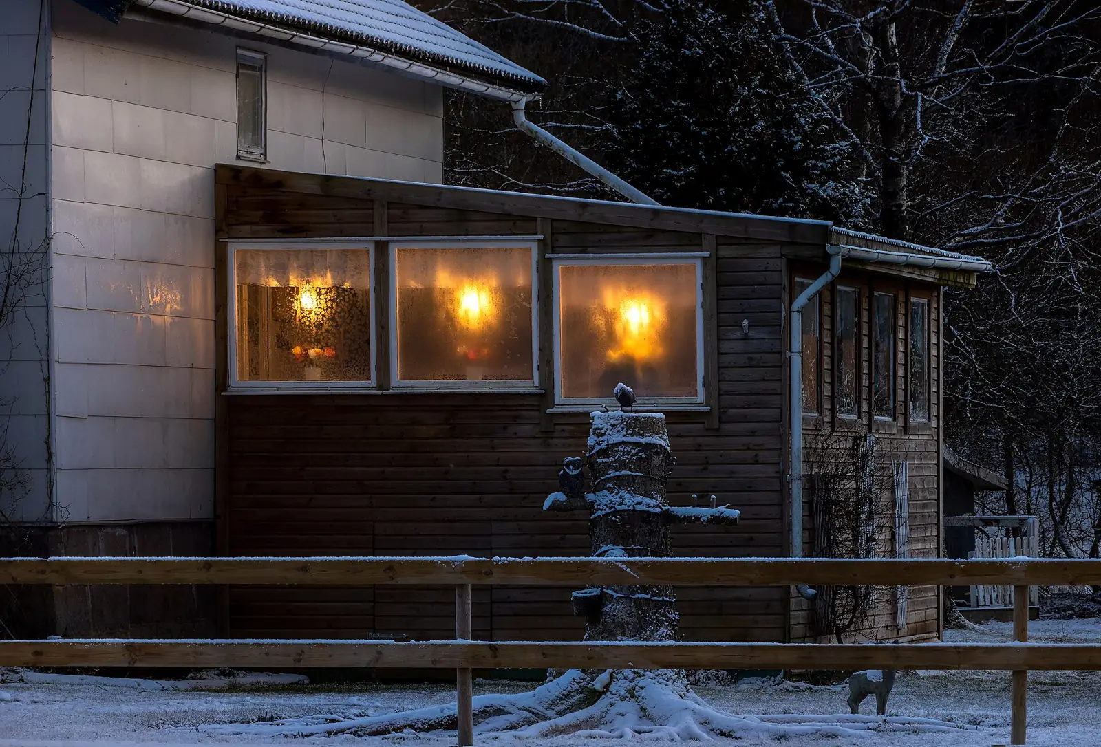 Varmt lampsken i fönstren på ett trähus en snöig vinterkväll