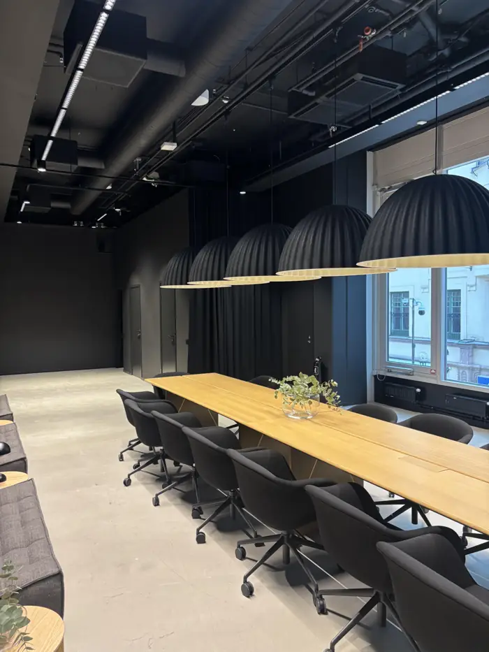 Fem stora svarta pendellampor i rad över ett långt konferensbord i en kontorslokal