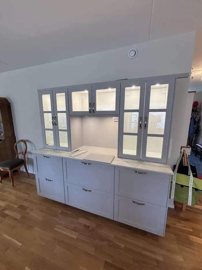 Ljust vitrinskåp med infällda LED-spotlights och bänkbelysning med uttag i ett hem